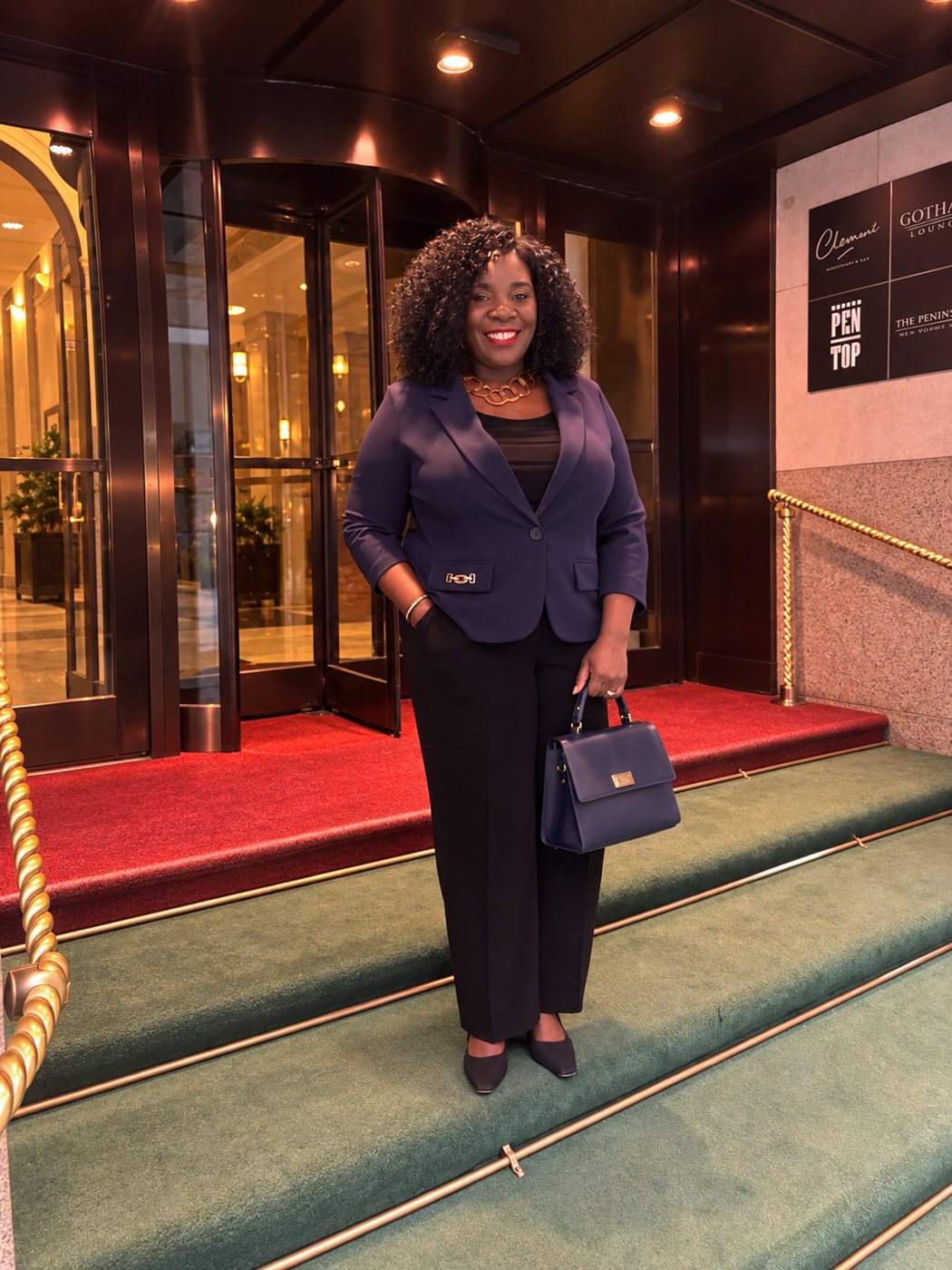 Clara Matonhodze smiling in a navy blazer on the steps of a New York hotel entrance