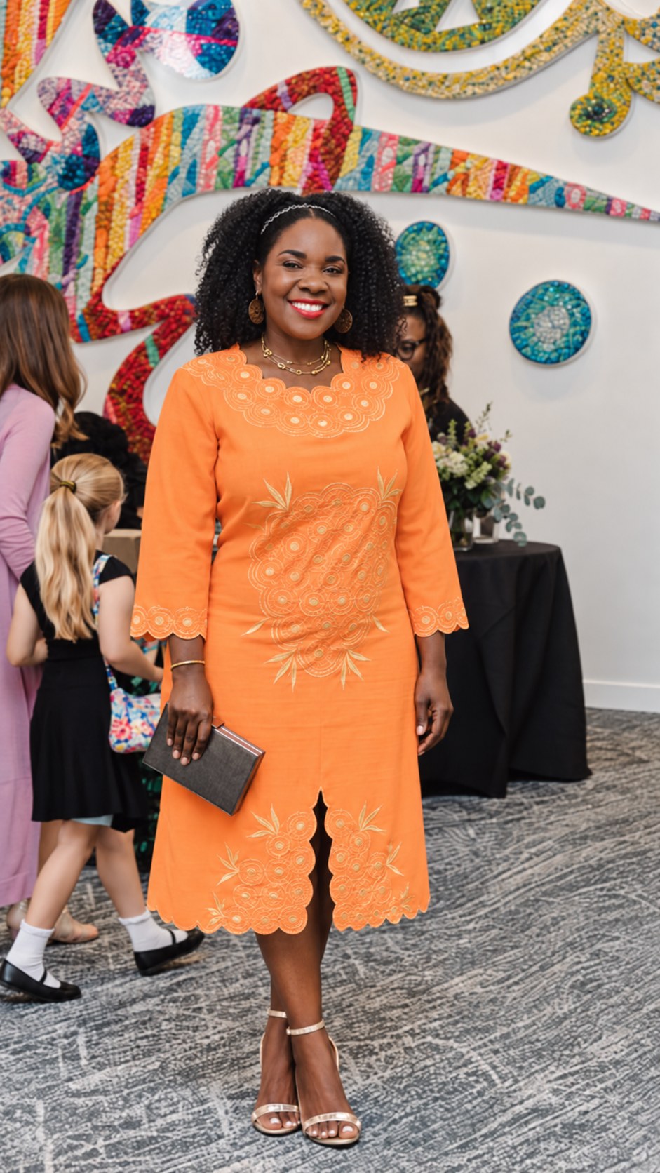 Clara Matonhodze, founder and principal consultant of The MCS Agency, smiling in an orange embroidered dress in front of a colorful mosaic mural