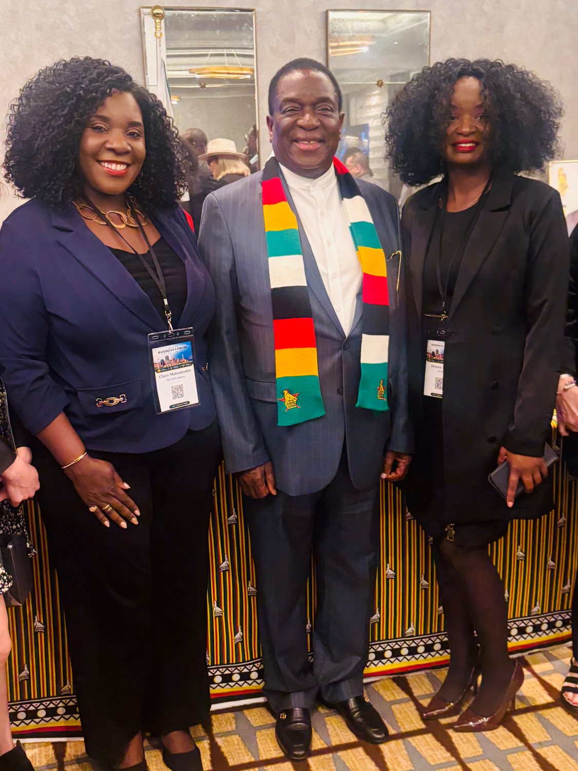 Clara Matonhodze wearing a business forum badge for The MCS Agency, standing beside a man in a Zimbabwe flag scarf and another woman