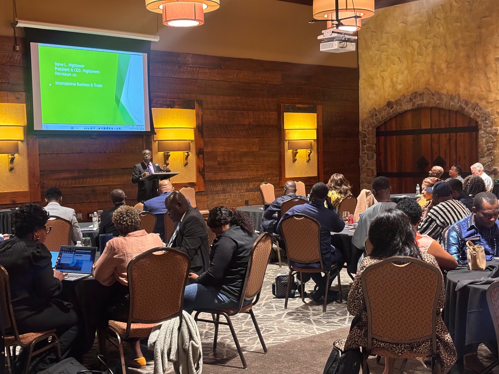 A speaker presenting on international business and trade to a seated audience in a banquet room