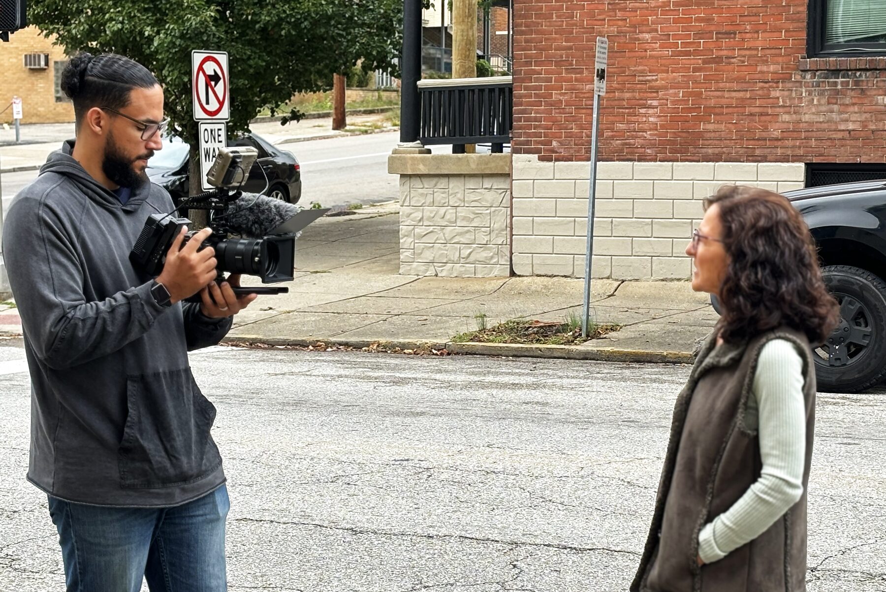 A videographer filming a woman on a city street corner